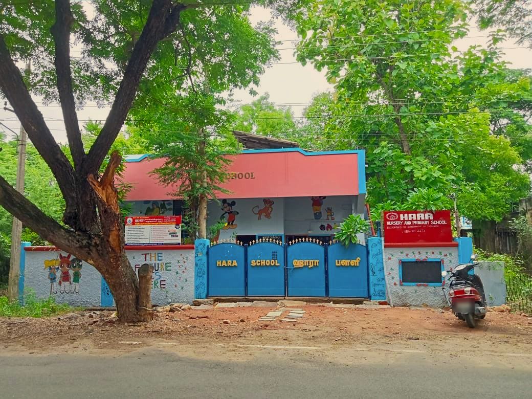 The front of Hara Nursery and Primary School: a blue gate marked Hara School in English and Tamil, painted cartoon walls, and a red signboard